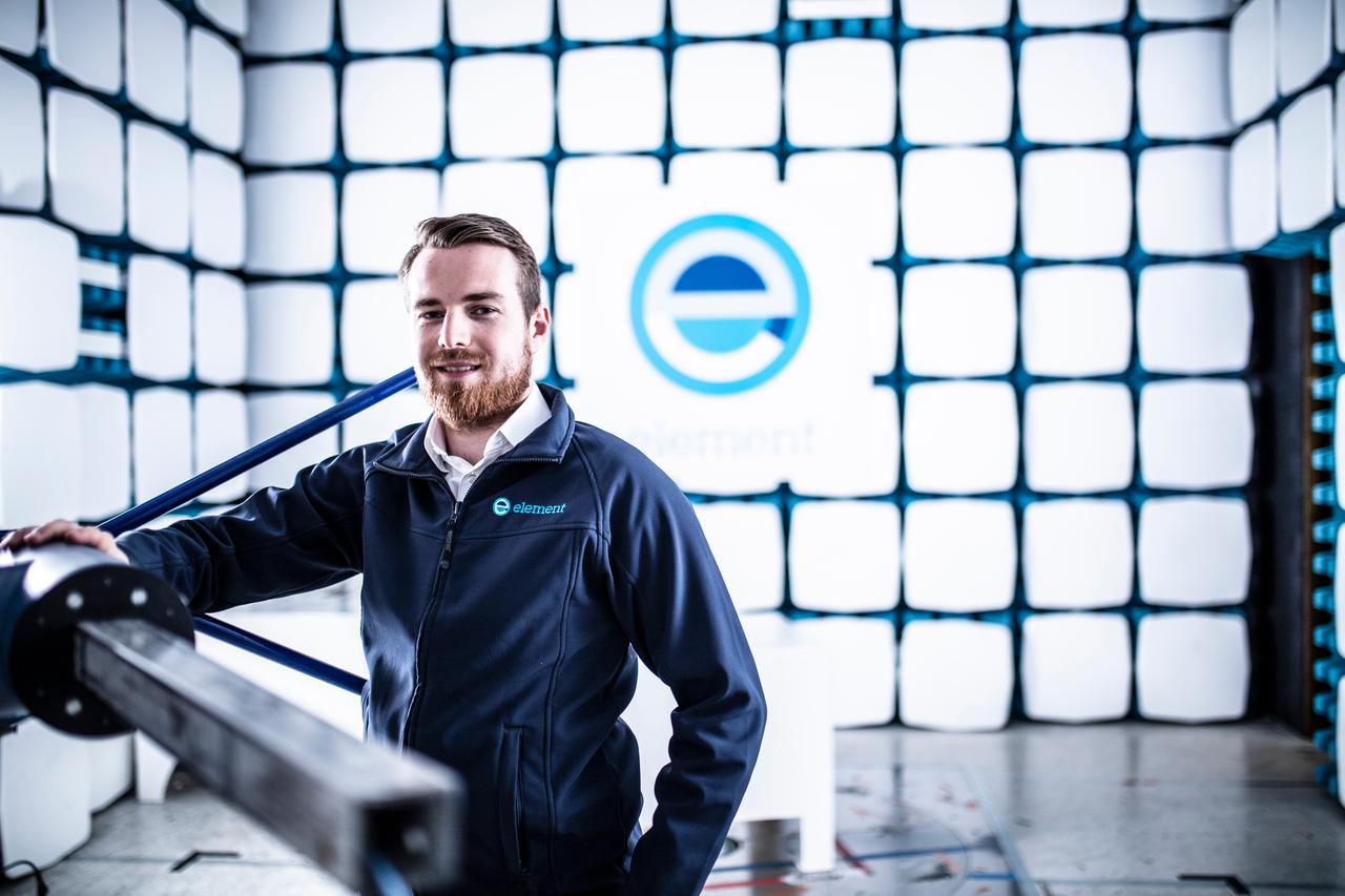 Testing engineer in an anechoic chamber with the Element E logo on the wall behind him