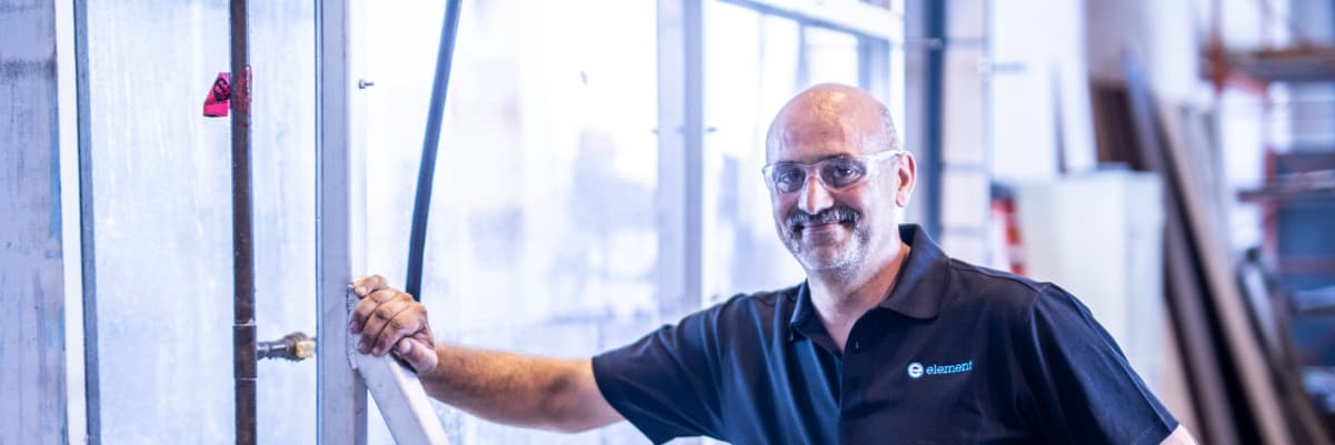 Element building products testing engineer in front of glass panel in industrial facility